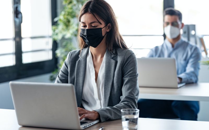 business partners wearing a hygienic face mask while working with laptops in the coworking space.