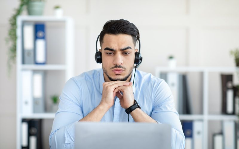 Worried millennial Arab man in headphones making online video call with business partner, having
